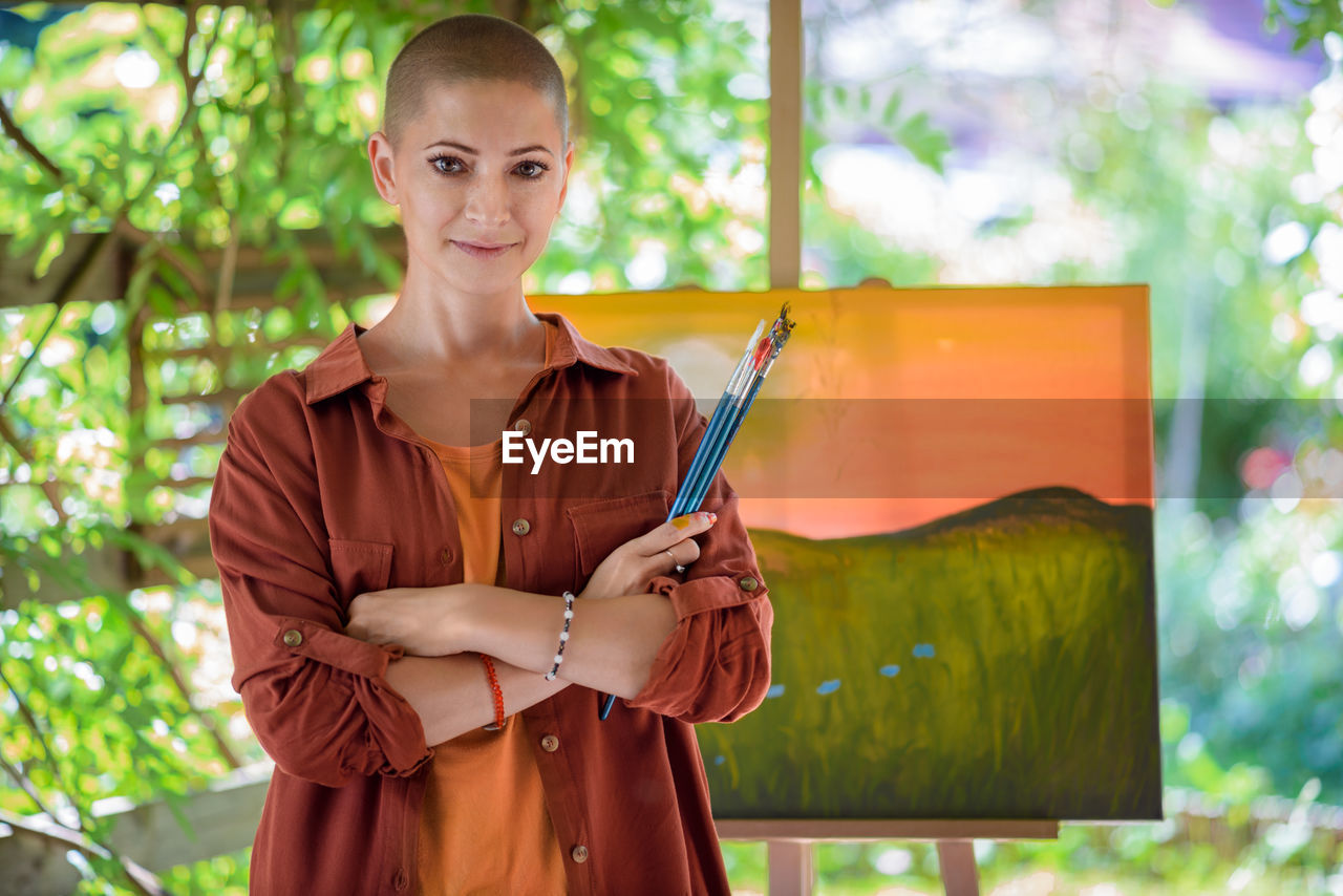 Beautiful young woman posing in front of her art canvas painting outdoors in her garden. 