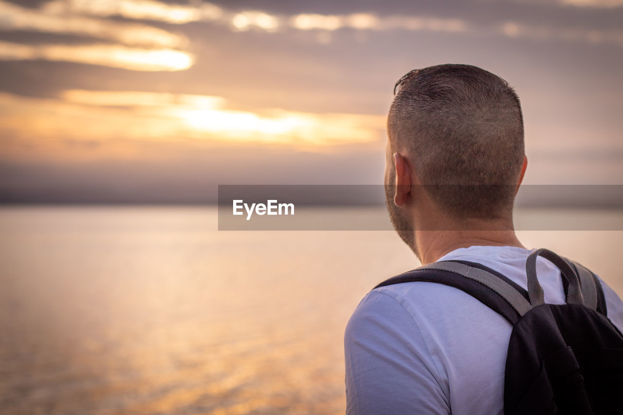 Rear view of man looking at sea against sky during sunset