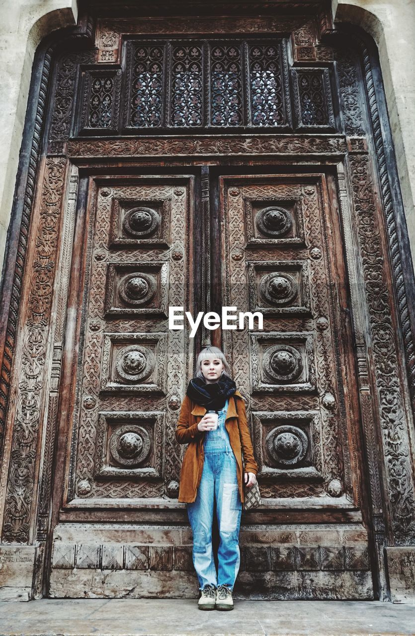 Full length of young woman standing against old-fashioned closed door