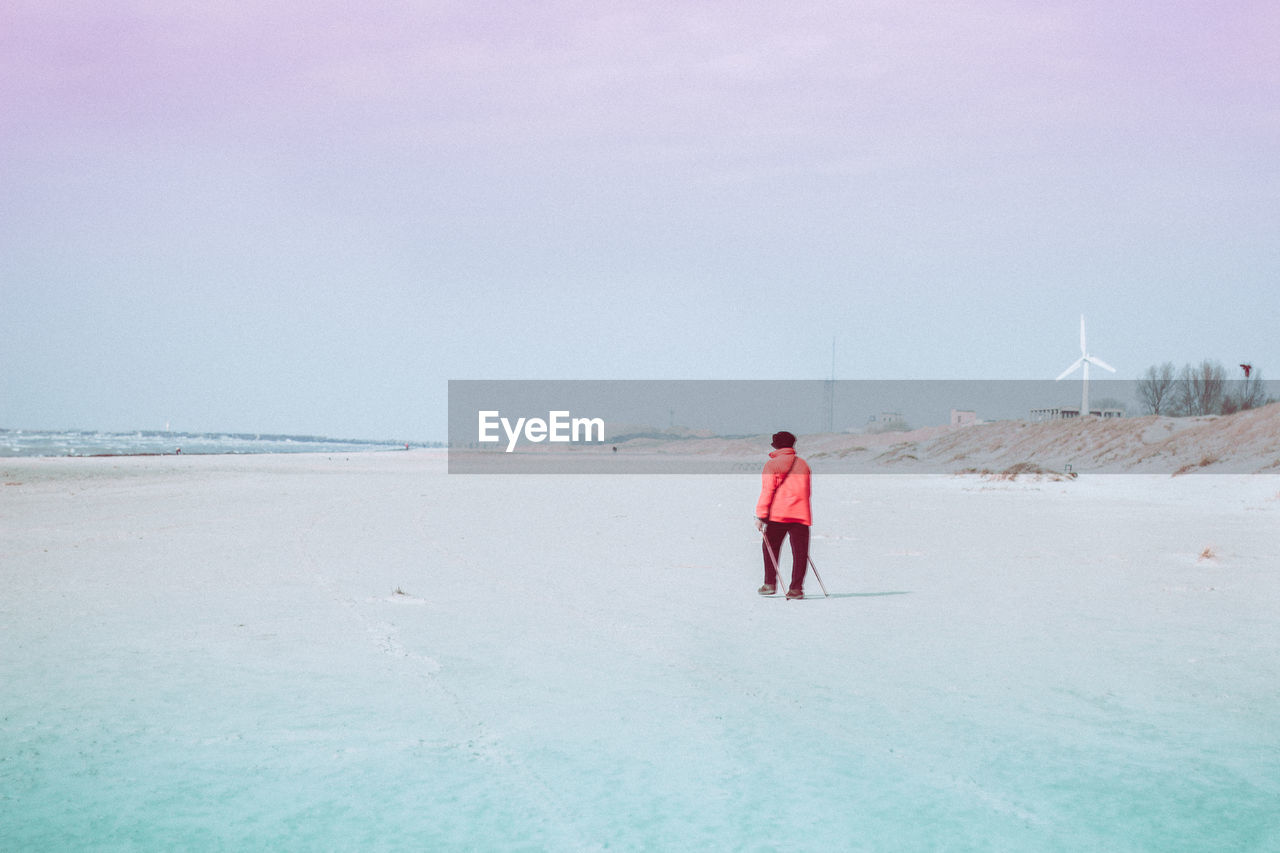 REAR VIEW OF MAN STANDING IN SEA AGAINST SKY