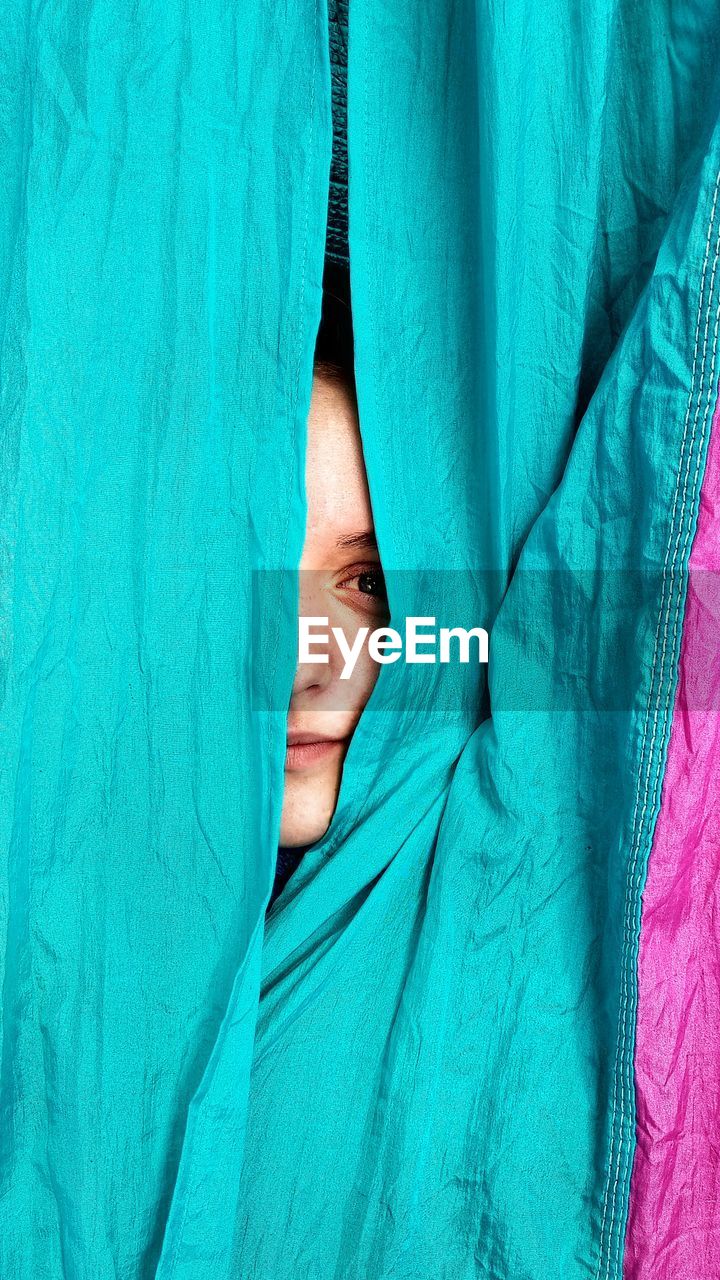 Close-up portrait of woman peeking through textile