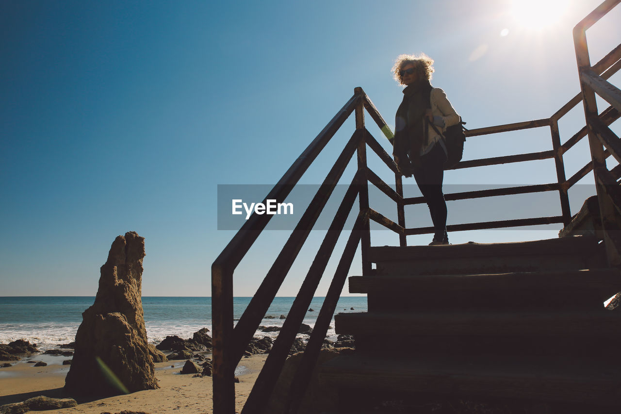 Woman standing on stairs at beach against sky