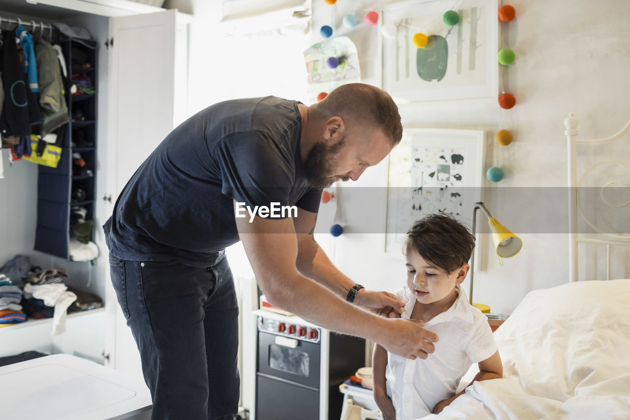 Man dressing son in bedroom