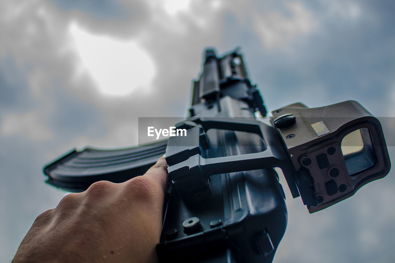 Close-up of hand holding gun against sky