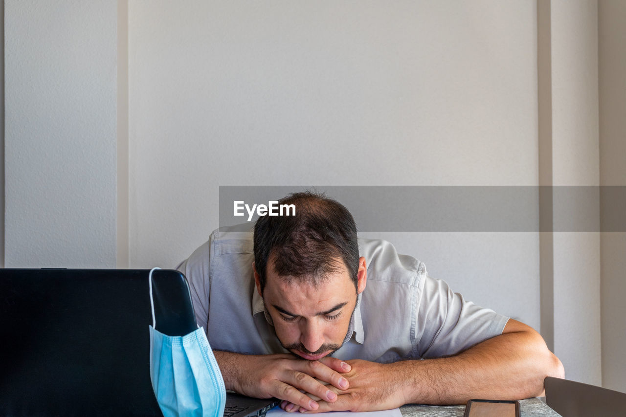 Frustrated man wearing flu mask sitting at office
