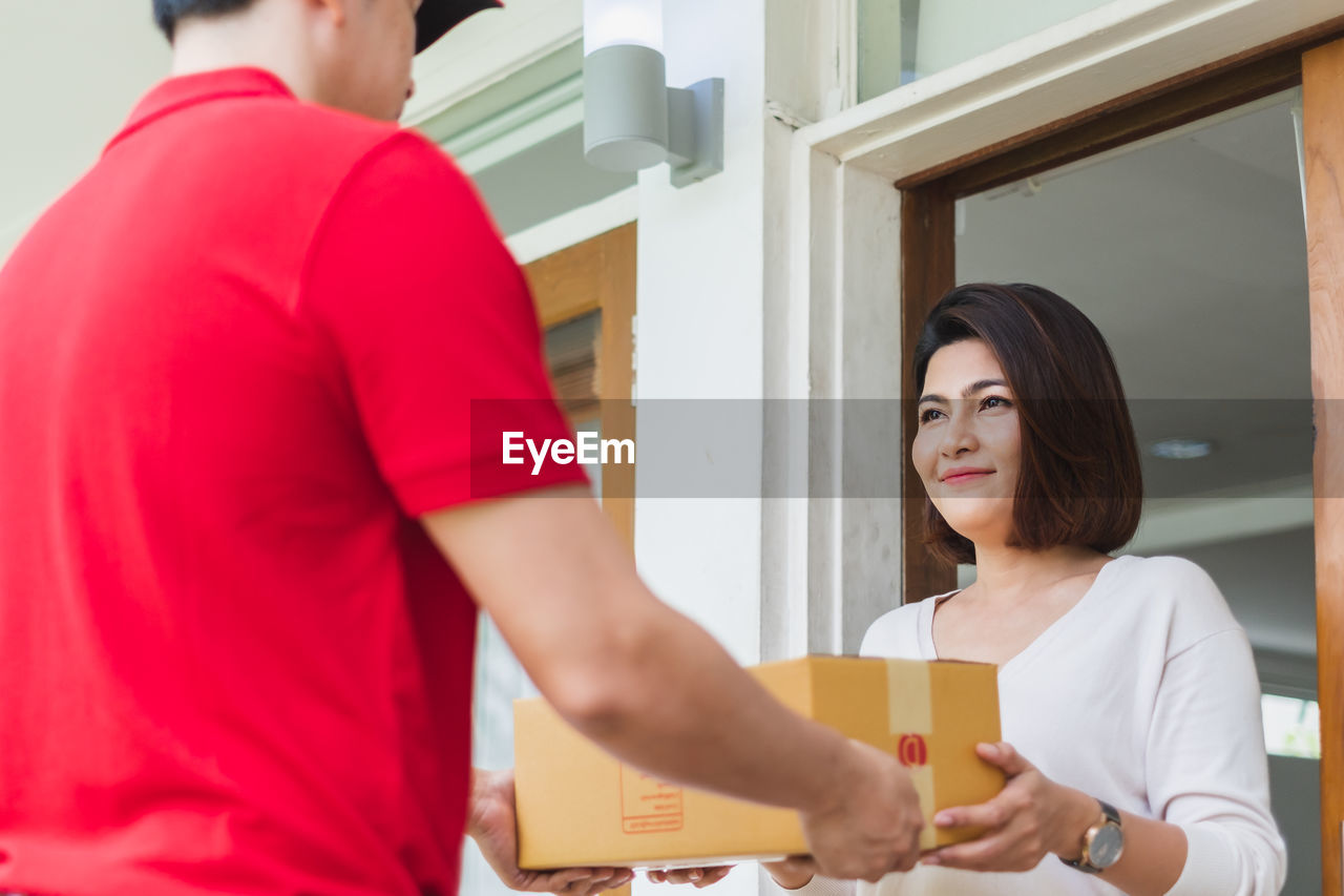 Woman holding mobile phone while receiving package from delivery man