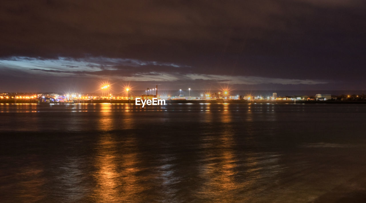 SCENIC VIEW OF ILLUMINATED CITY BY SEA AGAINST SKY