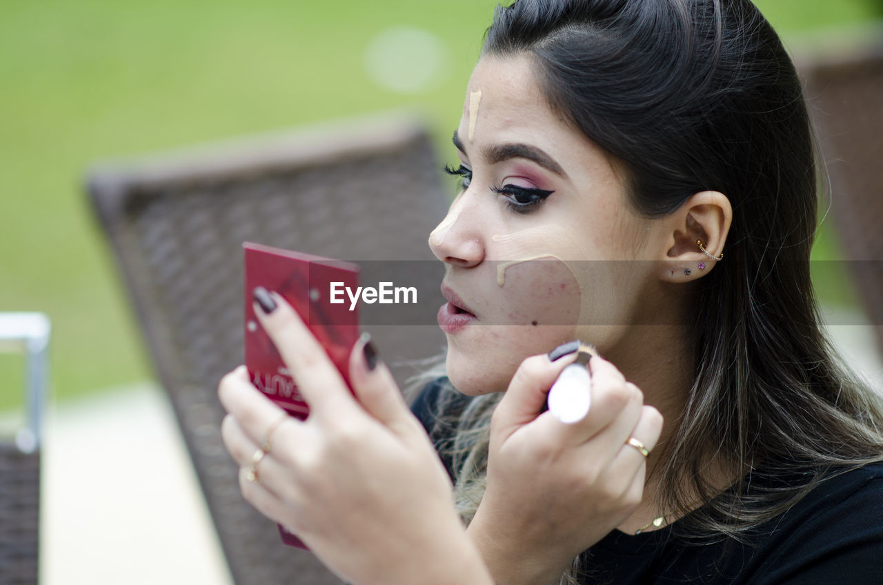 Close-up portrait of young woman putting on make-up