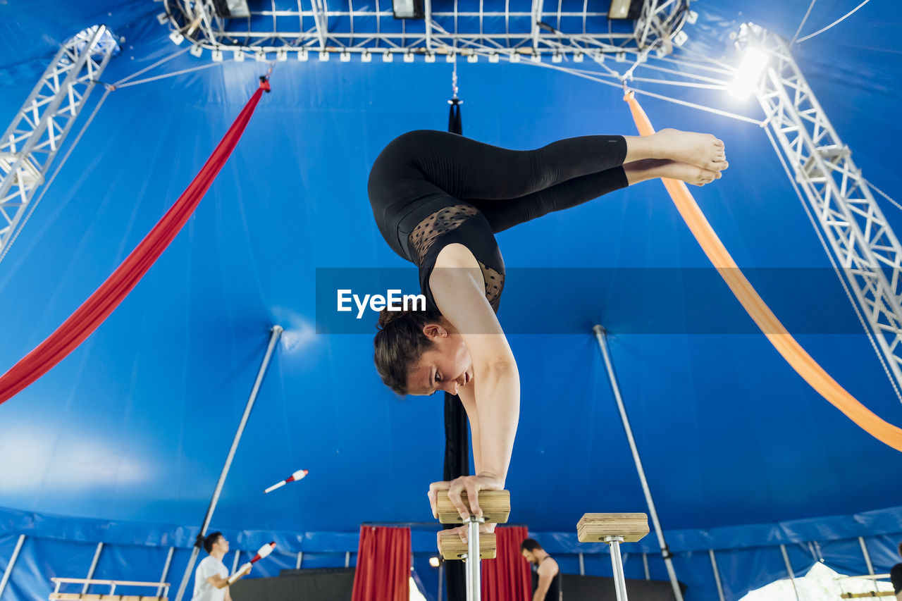 Female acrobat doing rehearsal on handstand cane with athletes in background