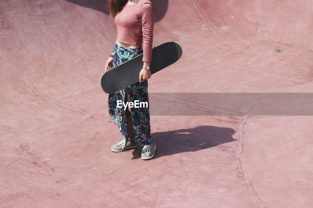 Low section of woman holding skateboard while standing at skateboard park