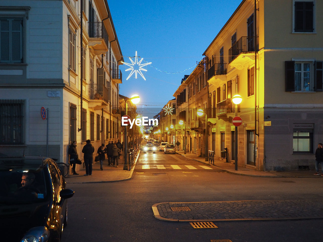 PEOPLE ON ILLUMINATED STREET AMIDST BUILDINGS AT NIGHT