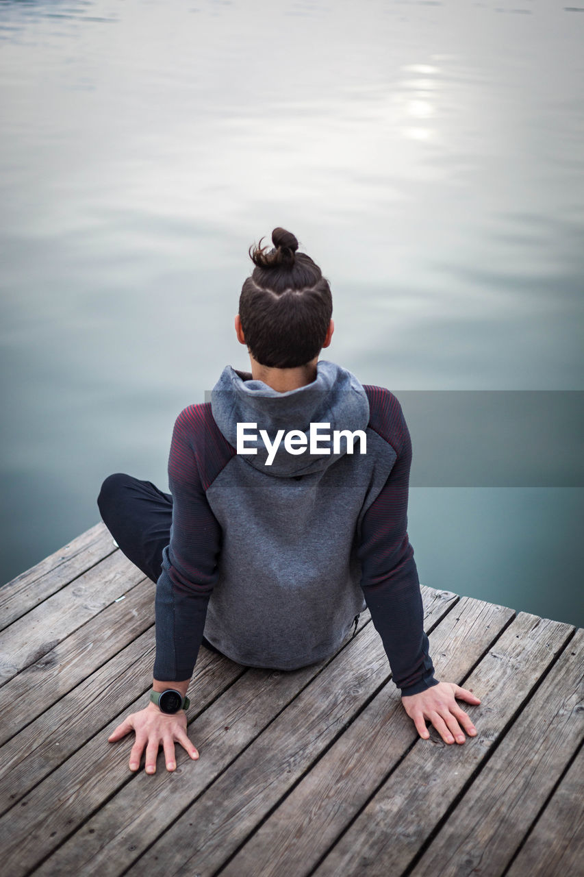 Rear view of woman sitting on pier over lake