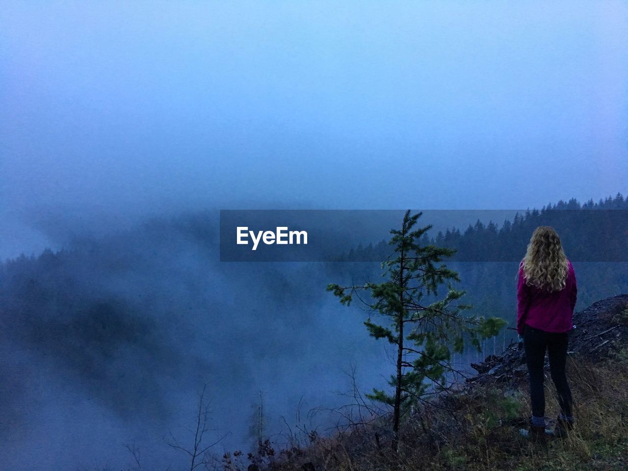 Rear view of woman standing on cliff against sky