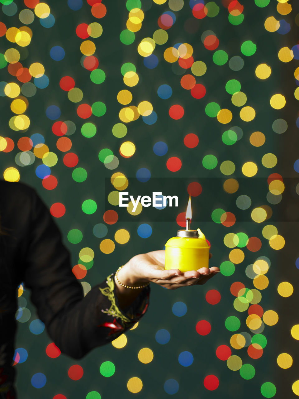 Cropped hand of woman holding oil lamp against illuminated christmas lights