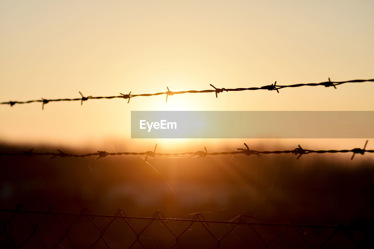 Barbed wire fence against sky during sunset