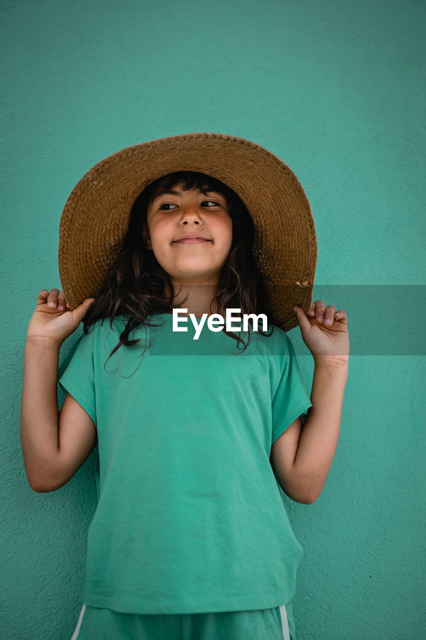 Portrait of girl in green t-shirt and straw hat against green wall