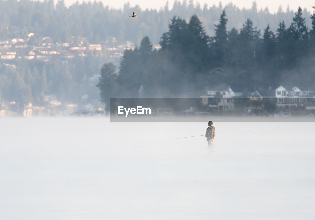 Person fishing in river during foggy weather
