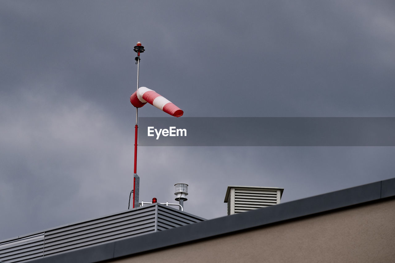 Windsock on rooftop against cloud-sky