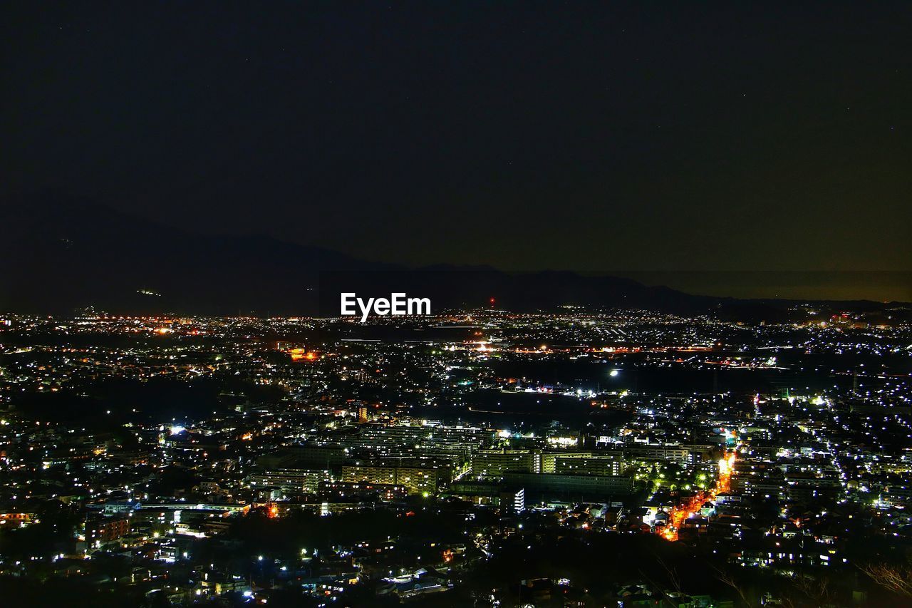 AERIAL VIEW OF ILLUMINATED CITYSCAPE AGAINST SKY AT NIGHT