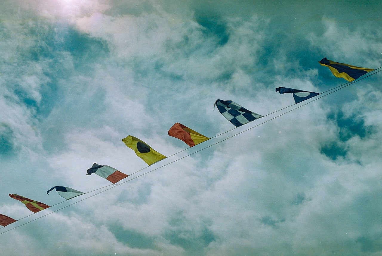 Low angle view of flags hanging on cable against sky