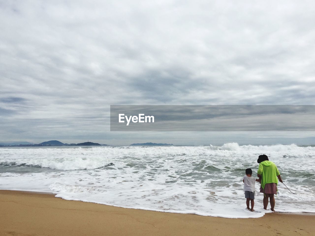 Rear view of mother and son standing at beach against sky