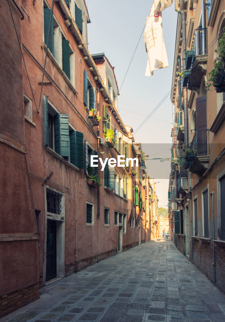 LOW ANGLE VIEW OF NARROW ALLEY AMIDST HOUSES