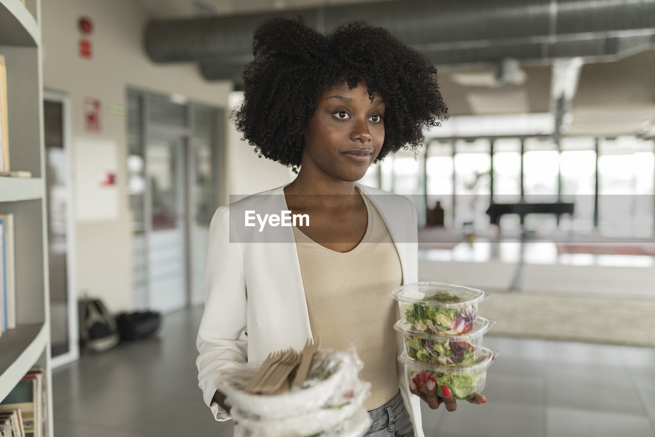 Young businesswoman with salad boxes standing in office