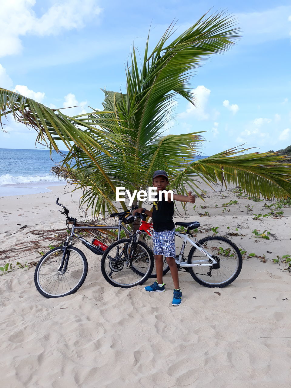 Portrait of boy with bicycle standing on beach against sky