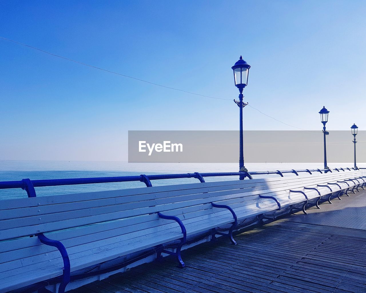 Street light by sea against clear blue sky