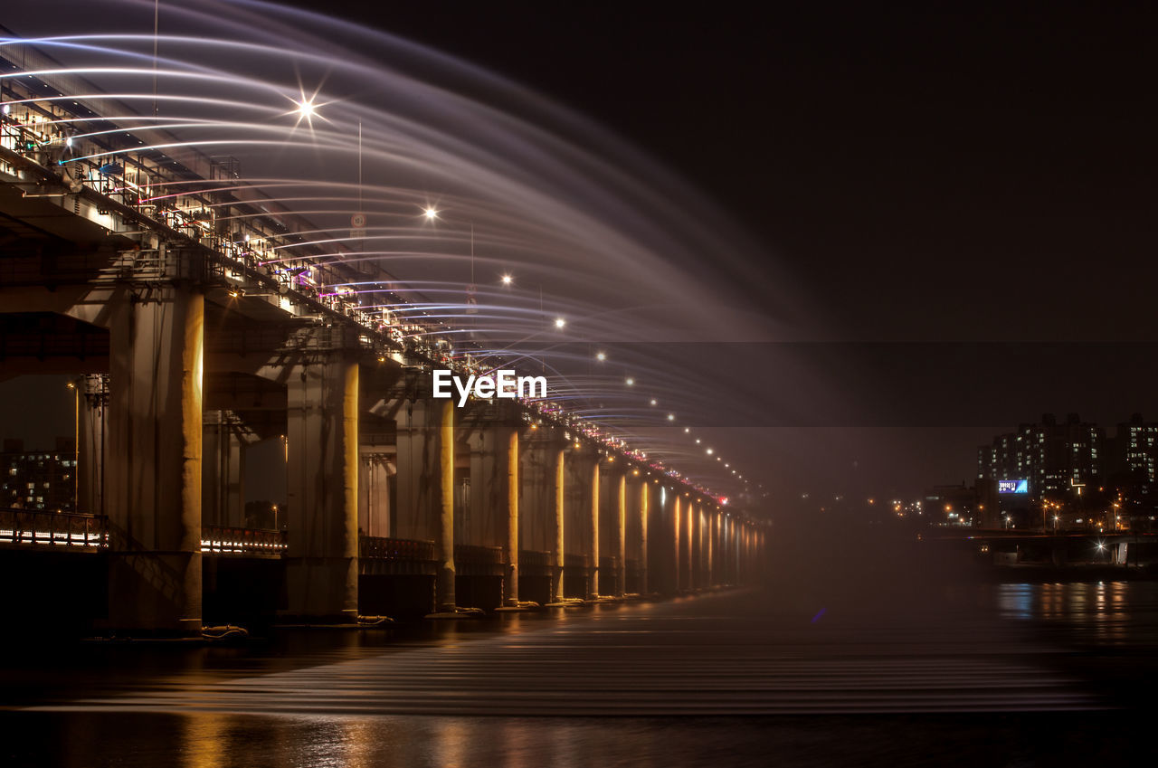 Low angle view of water flowing from bridge in river against sky at dusk