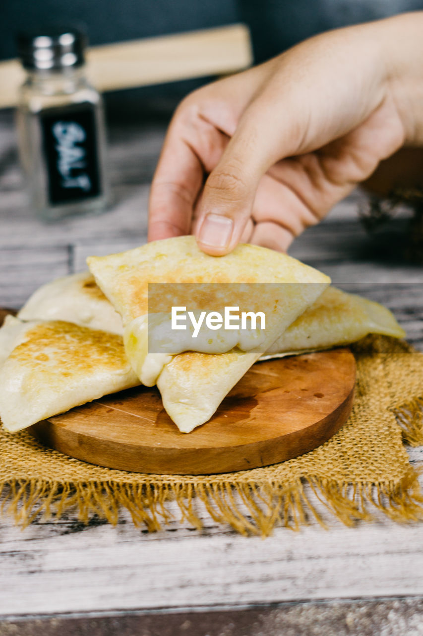 CLOSE-UP OF HAND HOLDING BREAD WITH KNIFE