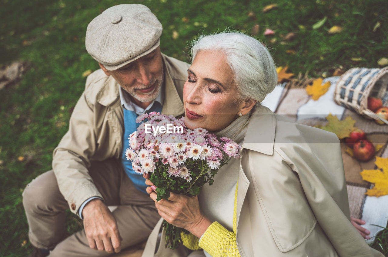 Senior woman holding bouquet while sitting with husband at park