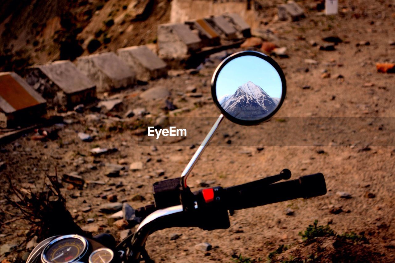 High angle view of mountain reflecting on motorcycle mirror at dirt road