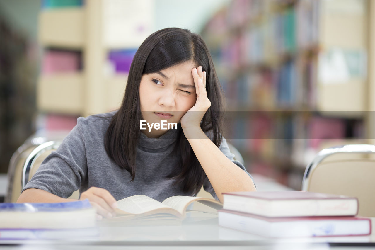 Young woman reading book while sitting at table in library