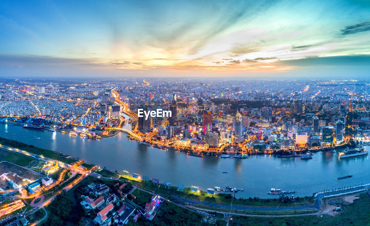 Aerial view of river by illuminated city during sunset