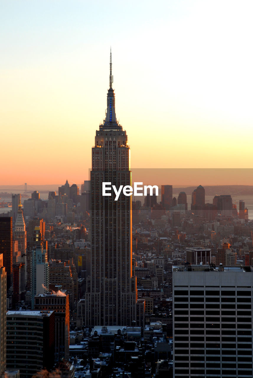 Empire state building amidst cityscape against sky during sunset