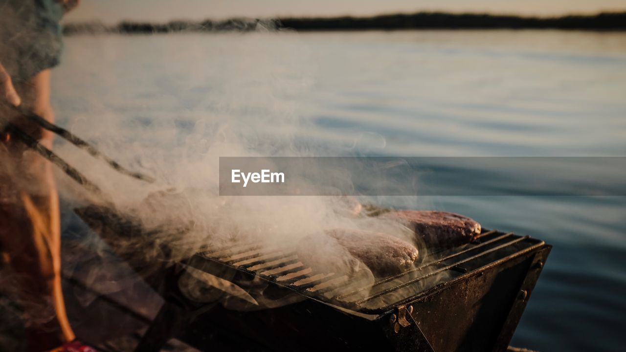 Close-up of meat cooking on barbecue grill by lake