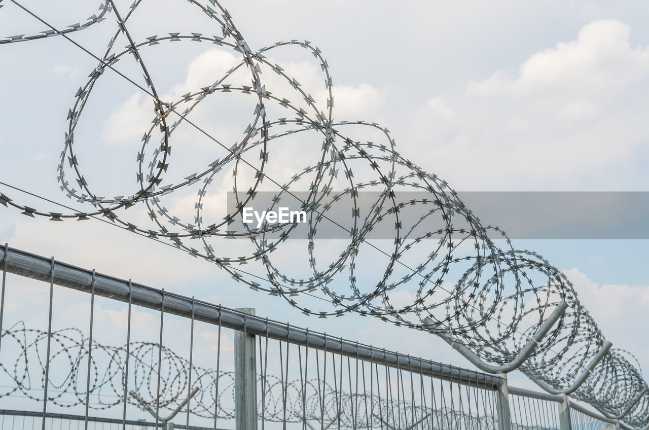 LOW ANGLE VIEW OF BARBED WIRE ON FENCE AGAINST SKY