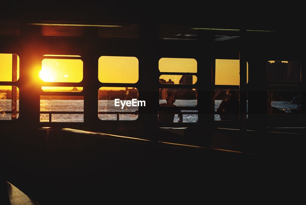 Silhouette people on ferry boat windows against river at sunset