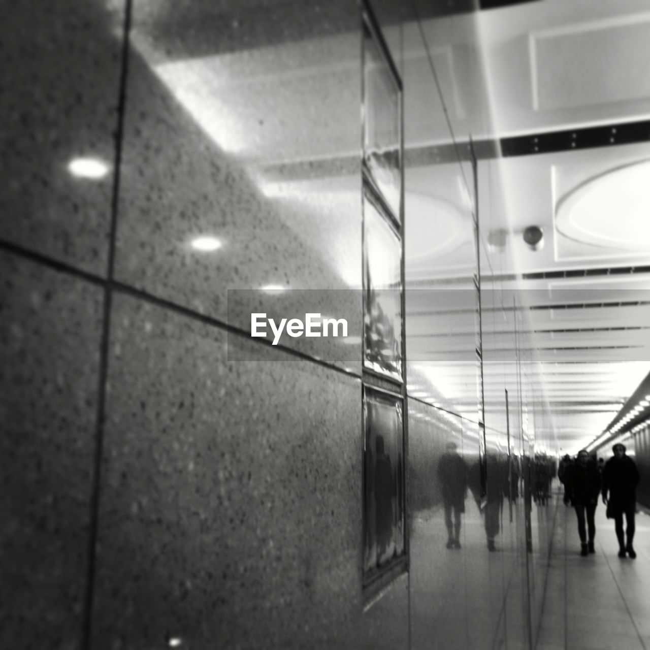 REFLECTION OF PEOPLE WALKING IN ILLUMINATED UNDERGROUND WALKWAY