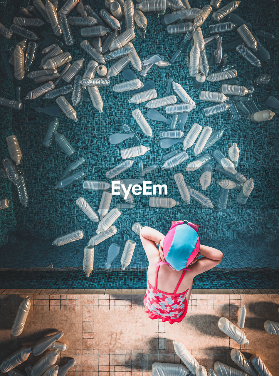 Directly above shot of girl standing by plastic bottles in swimming pool