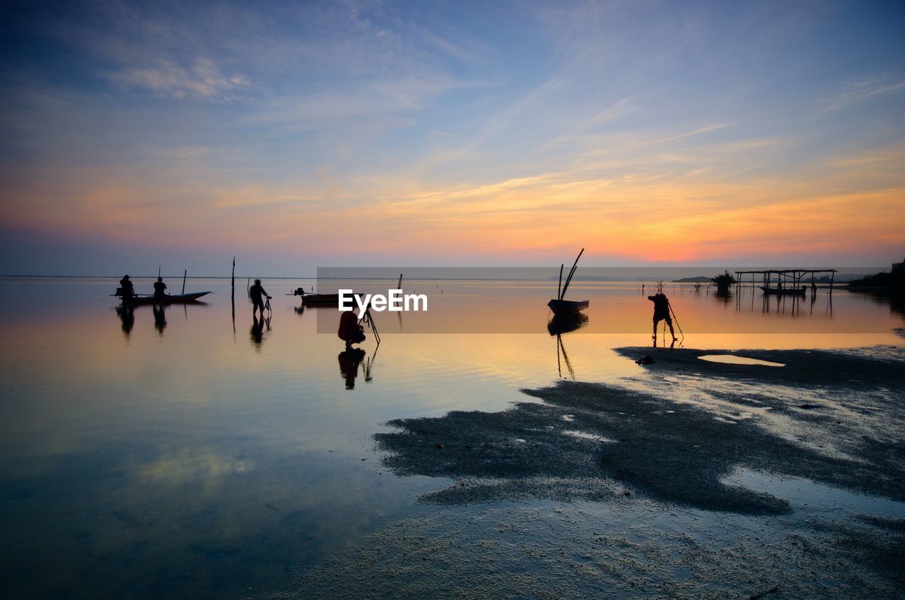 Silhouette wooden posts on beach against sky during sunset