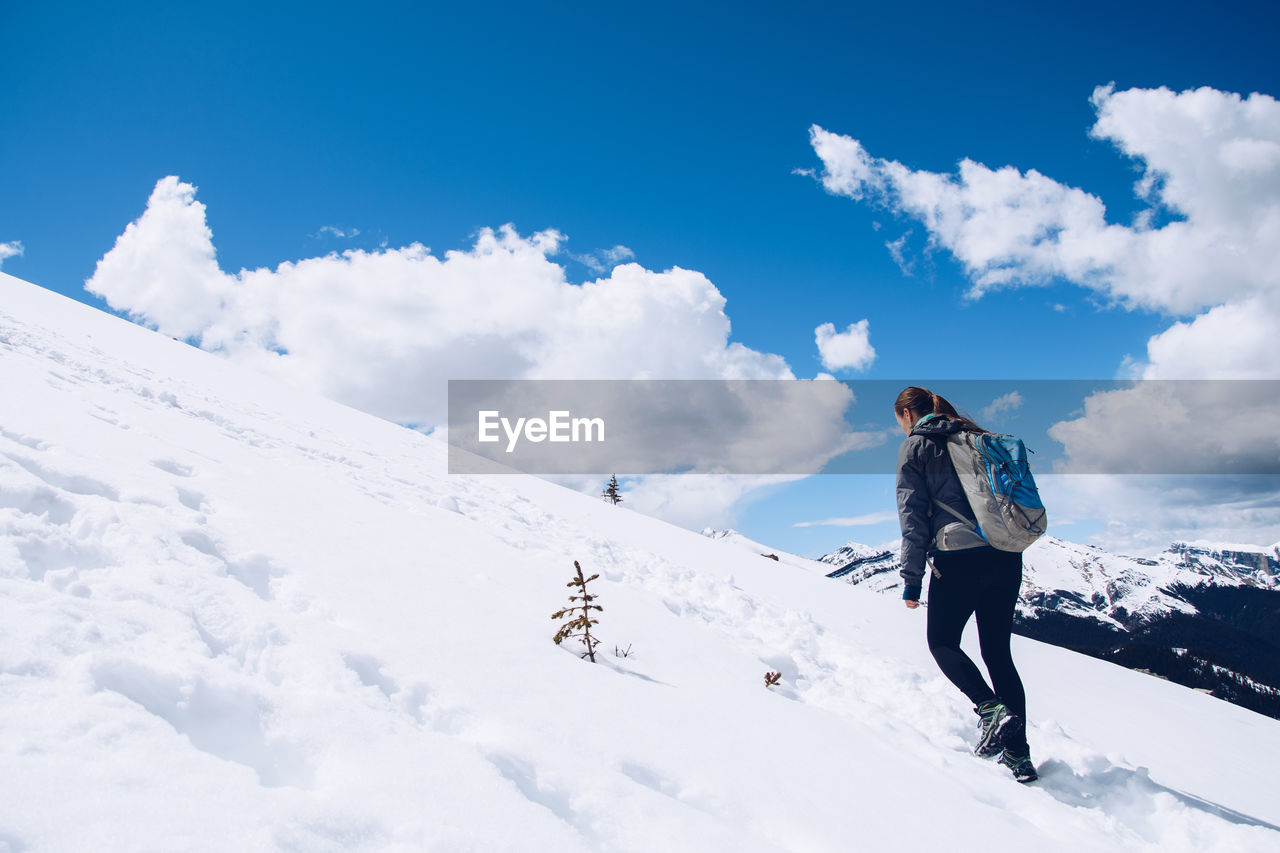 Rear view of woman walking on snowcapped mountain against sky