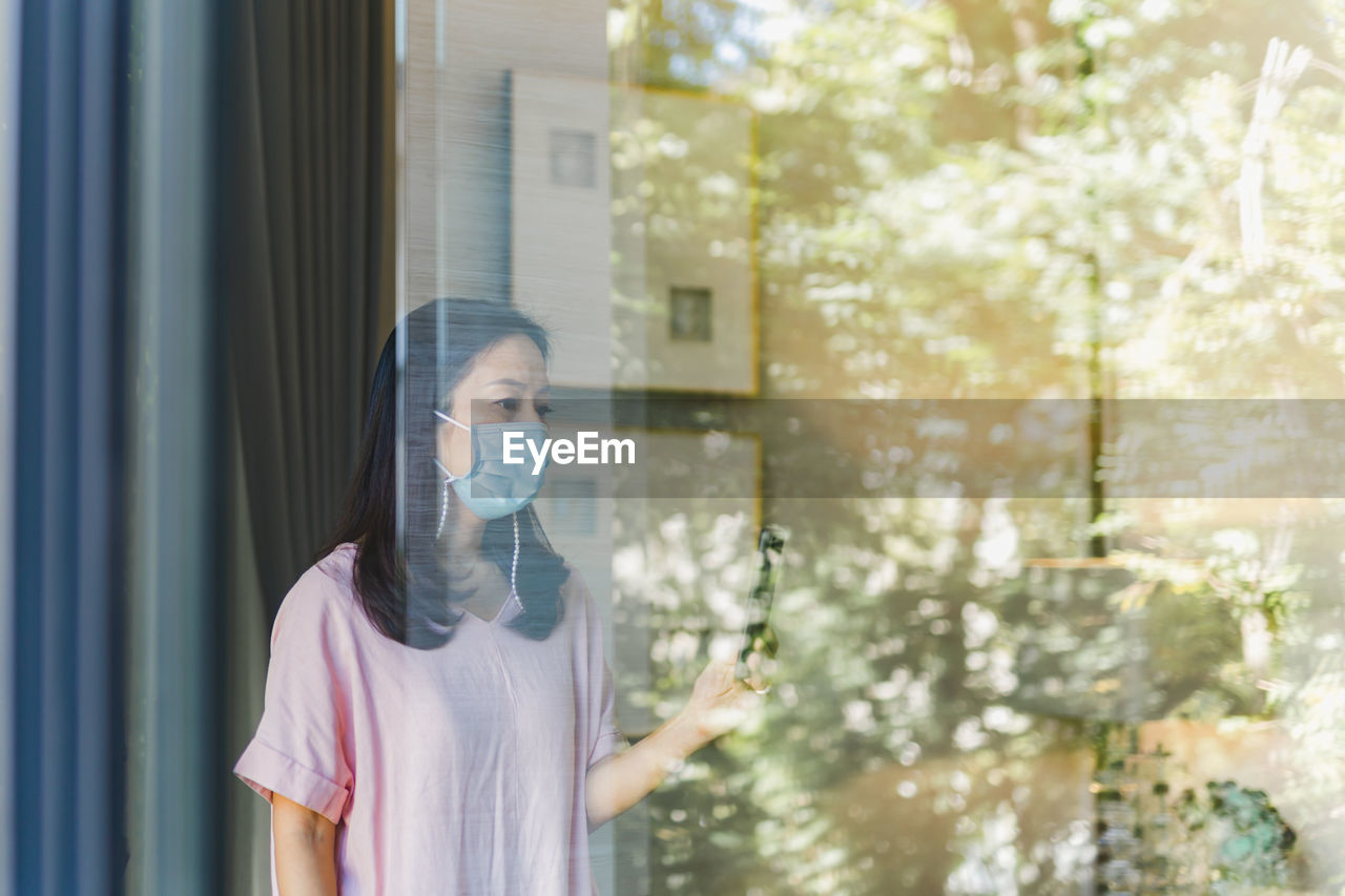 Woman looking through window while using smartphone 