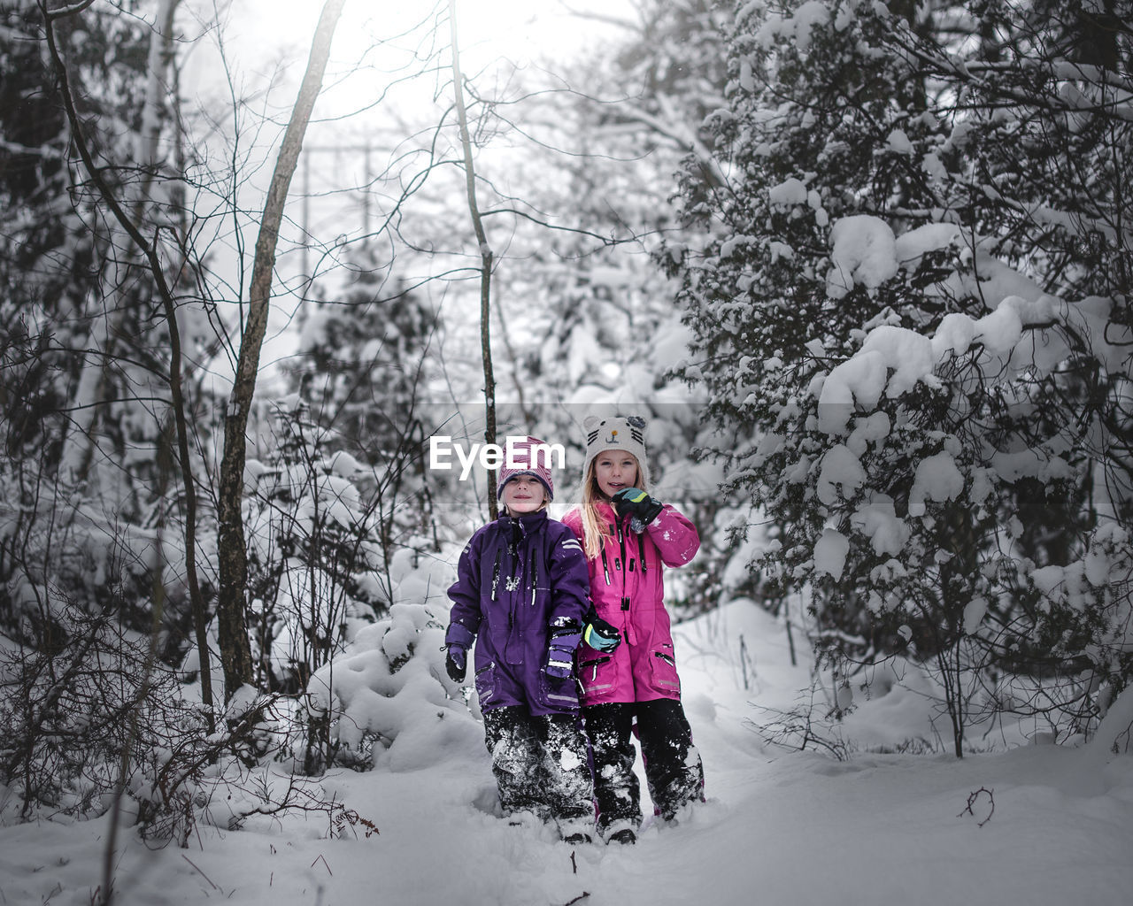 Portrait of sisters in warm clothing standing at snow covered forest