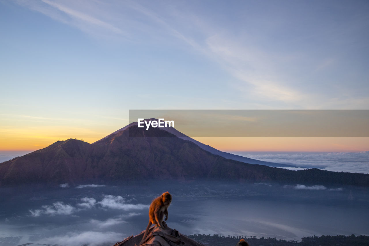 WOMAN WITH SNOWCAPPED MOUNTAIN AGAINST SKY DURING SUNSET