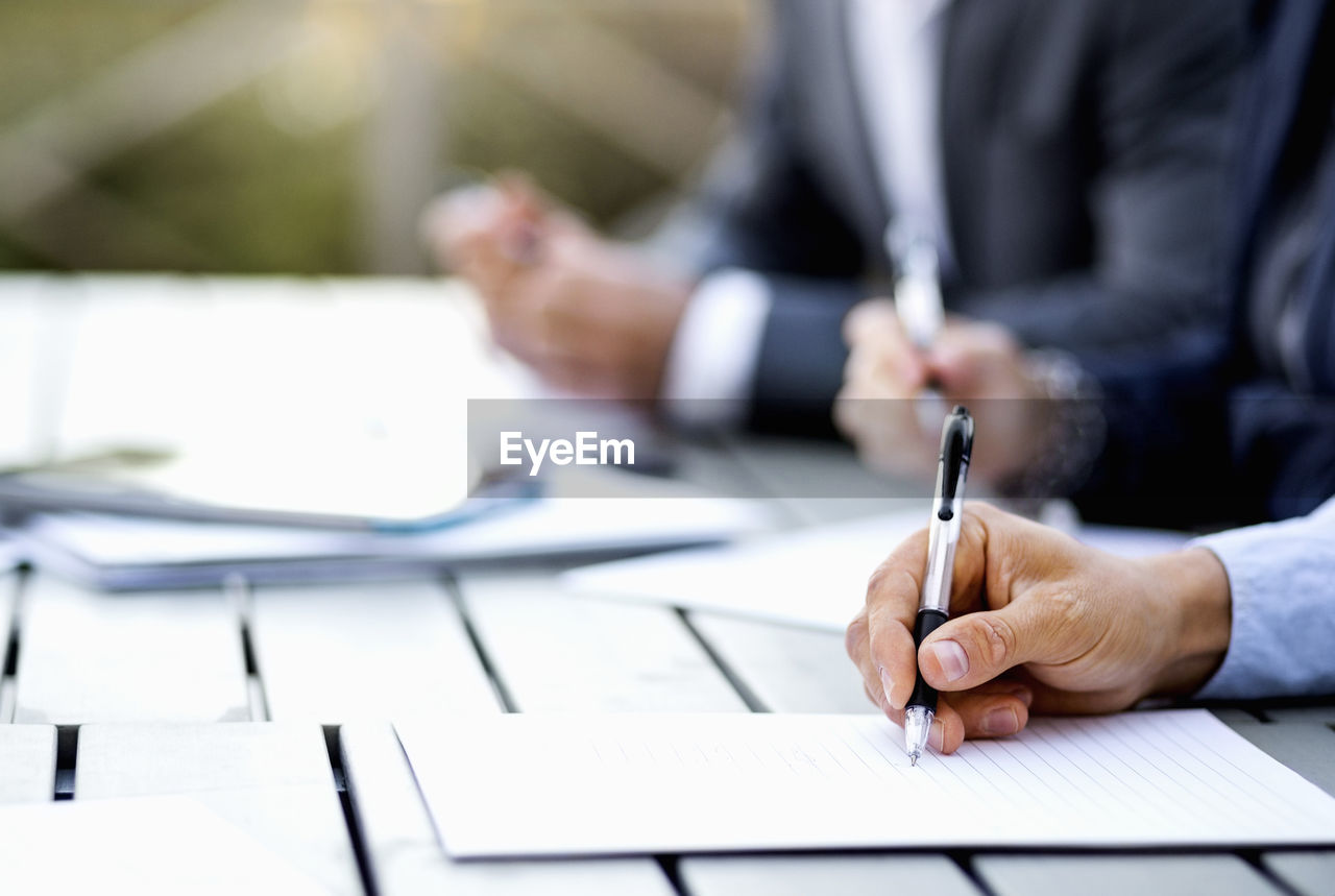 Cropped image of businessman writing on document at table