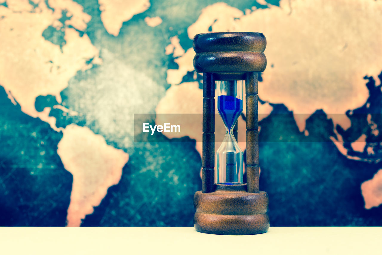 Close-up of hourglass against map on table