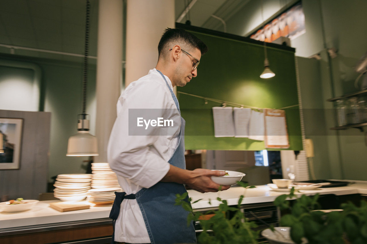 Side view of male chef holding bowls while walking in commercial kitchen