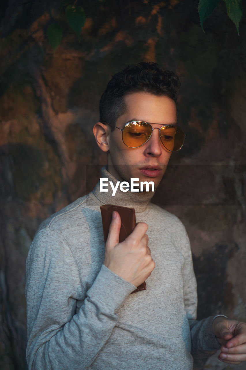 Young man wearing sunglasses while standing against wall